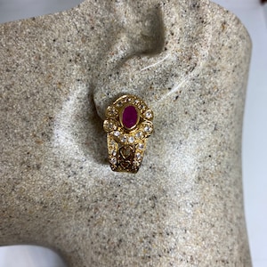 Op de afbeelding: Gouden oorbellen met een roze ovale steen omringd door heldere strass steentjes. De oorbellen hebben een delicaat, ingewikkeld ontwerp.