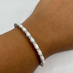 May include: A silver bracelet with white oval-shaped opals set in a continuous line. The bracelet is on a person's wrist.