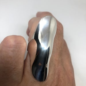 May include: A silver ring with a unique, abstract design. The ring is made of smooth, polished metal and has a curved, organic shape.