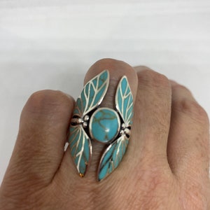 May include: A silver ring with a turquoise stone set in the center. The ring is designed with two wings on either side of the stone.