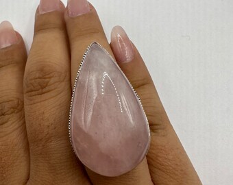 May include: A silver ring with a large, teardrop-shaped pink rose quartz stone.