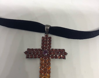 May include: A black velvet choker necklace with a silver cross pendant. The cross is adorned with red, orange, and purple gemstones.