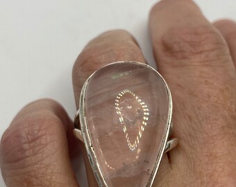 May include: A silver ring with a large, teardrop-shaped, light pink rose quartz stone.