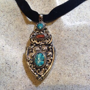 May include: A silver pendant necklace with a turquoise and coral stone design. The pendant is attached to a black velvet choker.