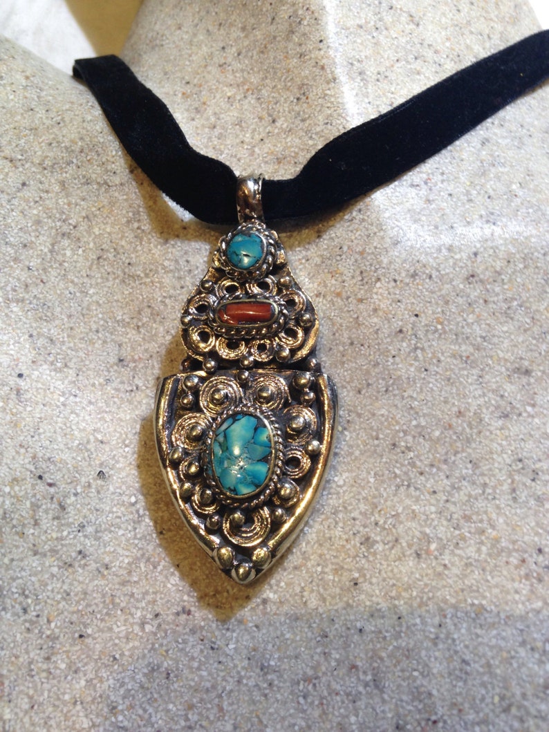 May include: A silver pendant necklace with a turquoise and coral stone design. The pendant is attached to a black velvet choker.