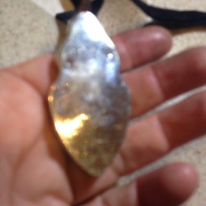 May include: A silver pendant shaped like a teardrop with a smooth, reflective surface.