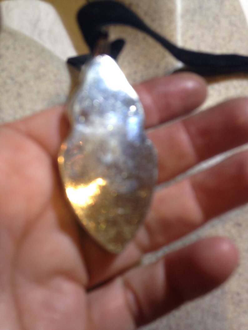 May include: A silver pendant shaped like a teardrop with a smooth, reflective surface.