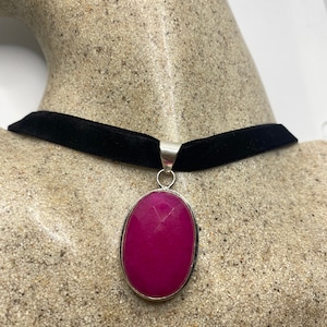 May include: A black velvet choker necklace with a silver pendant featuring a large oval-shaped pink gemstone.