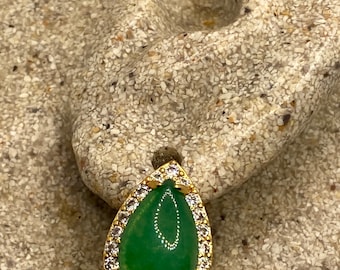 May include: A teardrop-shaped green gemstone earring with a gold setting and a row of clear cubic zirconia stones around the perimeter.