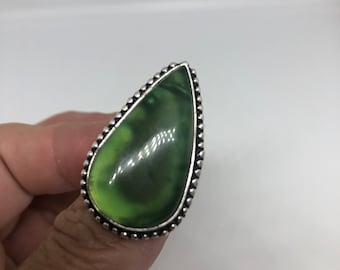 May include: A teardrop-shaped green stone ring with a silver setting. The ring has a beaded edge.