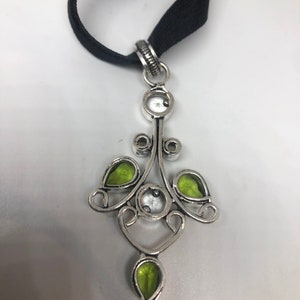May include: A silver pendant necklace with a black ribbon. The pendant features a delicate design with green and white gemstones.