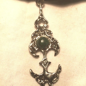 May include: A silver pendant necklace with a green stone set in a detailed, intricate design. The necklace is on a black velvet ribbon.