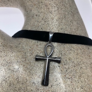 May include: A silver ankh pendant on a black velvet choker necklace.