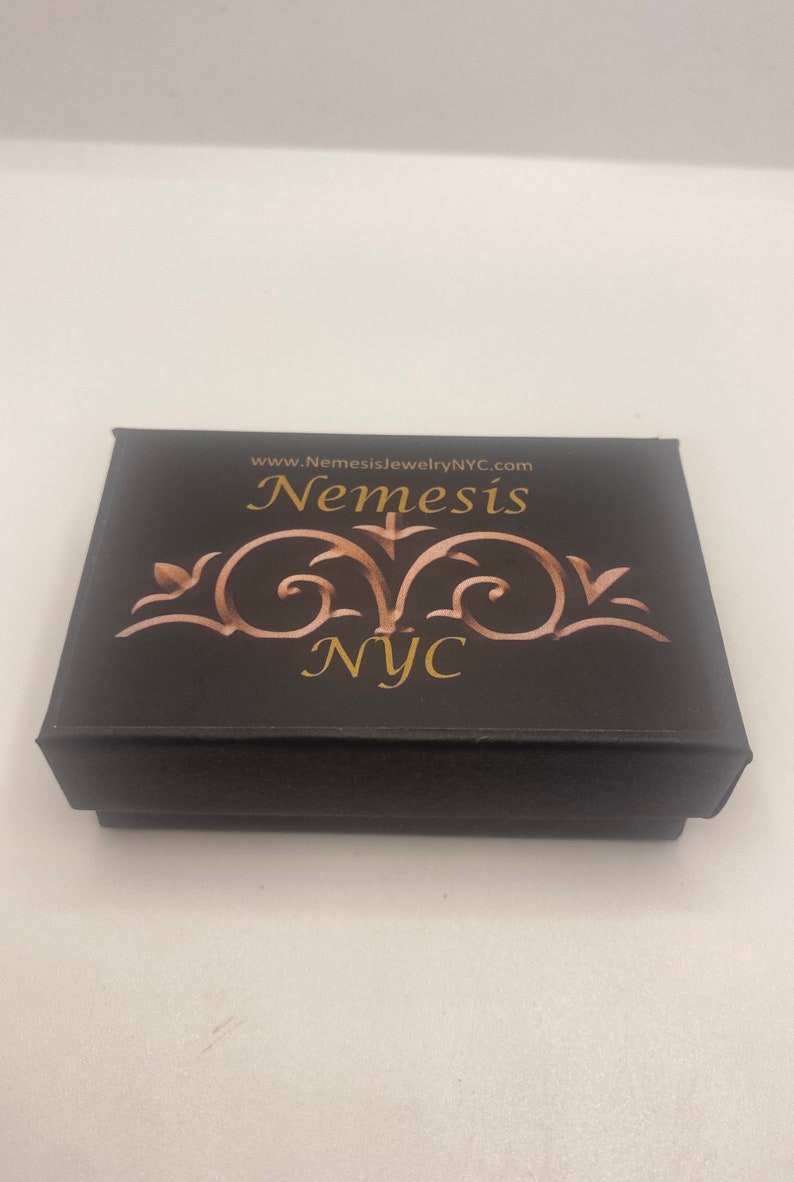 May include: Black jewelry box with gold lettering that reads "www.NemesisjewelryNYC.com Nemesis NYC".
