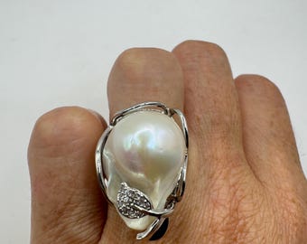 May include: A silver ring with a large white baroque pearl set in a leaf design with small clear diamonds.