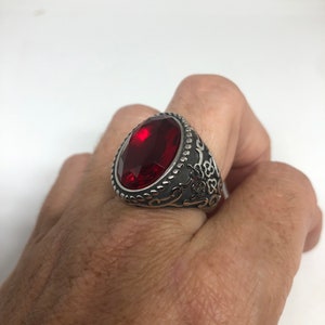 May include: A silver ring with an ornate design and a large, oval-shaped red gemstone.