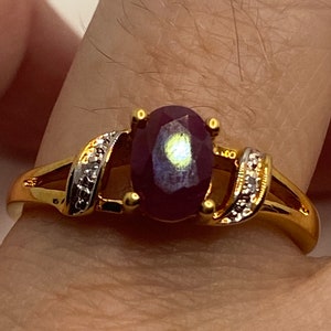 May include: A gold ring with a large oval-shaped ruby gemstone and smaller diamonds set in the band.