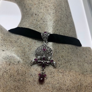 May include: A silver filigree pendant necklace with purple and white stones hangs from a black velvet choker.