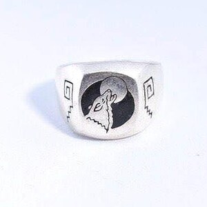 May include: A silver ring with a wolf howling at the moon design. The ring is square shaped and has a black and white design.