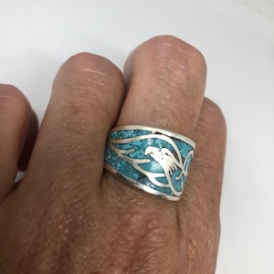May include: Silver ring with a turquoise inlay and an eagle design. The ring features a wide band with a detailed eagle head and wing design. The turquoise stones are set in a mosaic pattern.