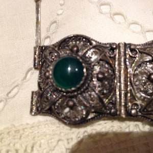 Puede incluir: Un brazalete de filigrana de plata con cierre de bisagra y tres piedras cabuj&oacute;n verdes.