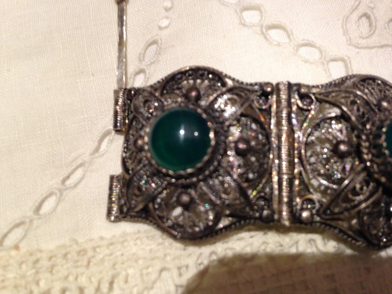 Puede incluir: Un brazalete de filigrana de plata con cierre de bisagra y tres piedras cabuj&oacute;n verdes.
