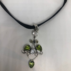 May include: A black velvet choker necklace with a silver pendant featuring clear and green gemstones.