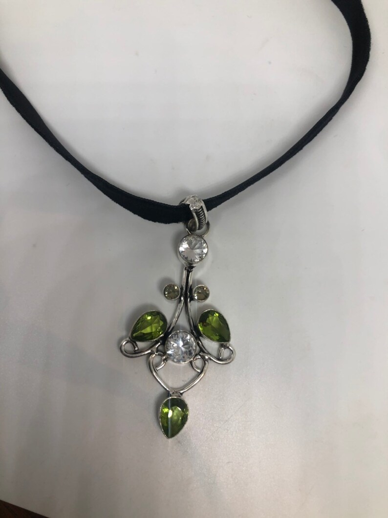 May include: A black velvet choker necklace with a silver pendant featuring clear and green gemstones.