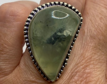 May include: A silver ring with a large, green, teardrop-shaped gemstone set in a beaded bezel.