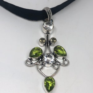 May include: A silver pendant necklace with a black velvet cord. The pendant features a delicate design with multiple green and clear gemstones.