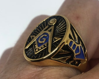May include: Gold ring with a black and blue Masonic symbol. The symbol is a compass and square with a 'G' in the center.