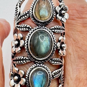 May include: A silver ring with three iridescent labradorite stones set in a floral design. The ring has a textured band and is adorned with delicate flower accents.