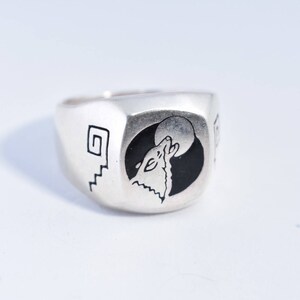 May include: A silver ring with a black and white design of a wolf howling at the moon. The ring has a geometric design on the side.