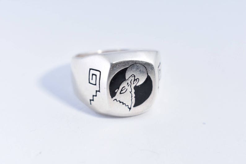 May include: A silver ring with a black and white design of a wolf howling at the moon. The ring has a geometric design on the side.