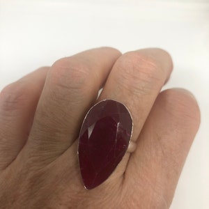 May include: A silver ring with a large, teardrop-shaped, dark red gemstone.