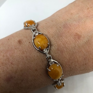 May include: A silver bracelet with four oval-shaped amber stones set in silver. The stones are surrounded by smaller clear stones.
