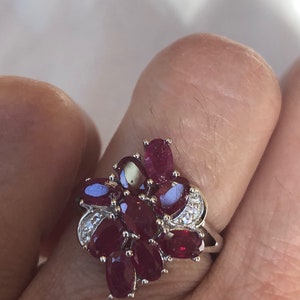 May include: A silver ring with a cluster of red ruby stones and small white diamonds.