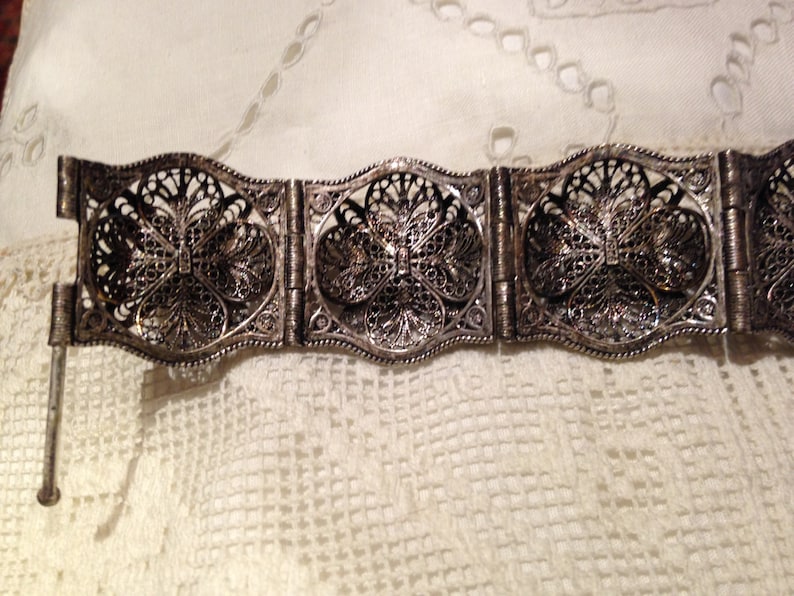 Puede incluir: Un brazalete de filigrana de plata con un delicado dise&ntilde;o floral. El brazalete est&aacute; hecho de varias secciones que est&aacute;n conectadas por bisagras.