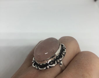 May include: A silver ring featuring a large oval rose quartz stone set in an ornate silver bezel. The ring is worn on a finger.