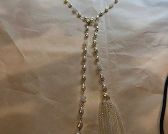 May include: A long white pearl necklace with two white pearl tassels. The necklace is made of small, round pearls and is strung on a silver chain.