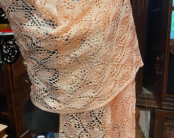Könnte beinhalten: Ein zartes, pfirsichfarbenes gestricktes Tuch mit einem Spitzenmuster. Das Tuch ist über eine Schaufensterpuppe gelegt.