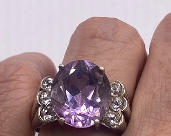 May include: A silver ring with a large oval-shaped amethyst gemstone surrounded by smaller clear gemstones.