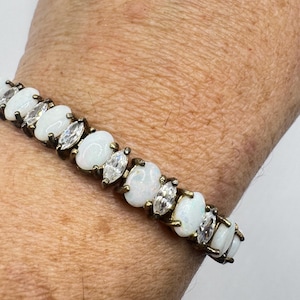 May include: A gold-toned bracelet featuring oval and marquise-cut white gemstones. The bracelet is composed of alternating oval-shaped white stones and marquise-cut clear stones, set in a gold-colored metal.