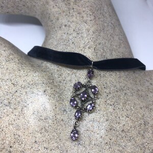May include: A black velvet choker necklace with a silver pendant featuring a cluster of purple gemstones.