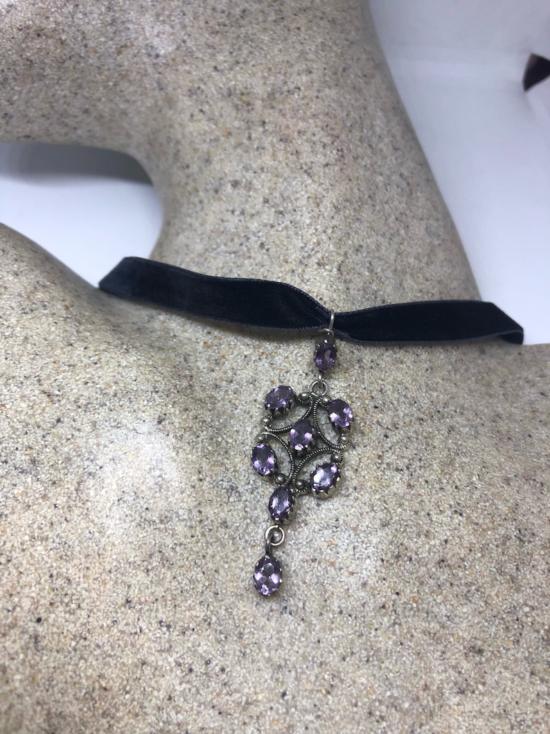 May include: A black velvet choker necklace with a silver pendant featuring a cluster of purple gemstones.