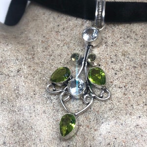 May include: A silver pendant necklace with a black velvet choker. The pendant features a delicate silver design with clear and green gemstones.