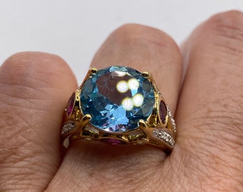 May include: A gold ring with a large oval blue topaz gemstone surrounded by smaller pink and white gemstones.