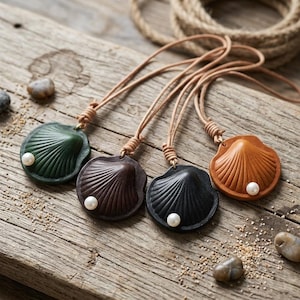 May include: Four shell-shaped pendants made of leather in green, dark brown, black, and tan. Each pendant features a single white pearl accent and is attached to a thin, light brown leather cord with a knotted detail at the top of the shell.