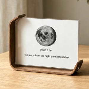Könnte beinhalten: Ein Holzfotorahmen mit geschwungenem Design, der ein Schwarz-Weiß-Bild des Mondes enthält. Das Bild enthält das Datum 2008.7.16 und den Text "The moon from the night you said goodbye."