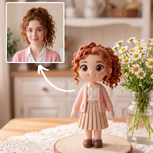 Può includere: Una statuetta personalizzata raffigurante una persona con capelli ramati ricci, che indossa un cardigan rosa chiaro sopra una camicia bianca con colletto, una gonna a pieghe beige e scarpe marroni. La statuetta poggia su una base in legno accanto a un vaso di margherite.